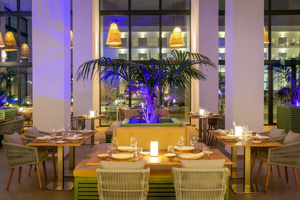 Un restaurante con mesas dispuestas para comer, destacando una planta decorativa en el centro e iluminación ambiental.