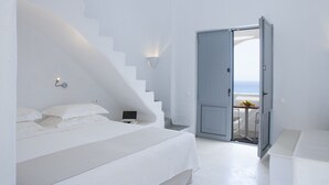 Un dormitorio minimalista con una cama, un escritorio y vista al mar por una puerta abierta.