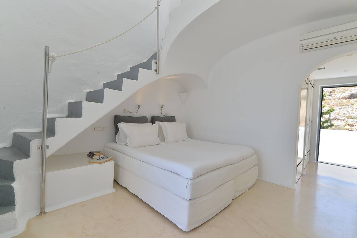 A bedroom with a white bed, a staircase with white walls, and a view through a glass door.