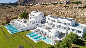Un resort moderno con varias piscinas, arquitectura blanca y montañas al fondo.
