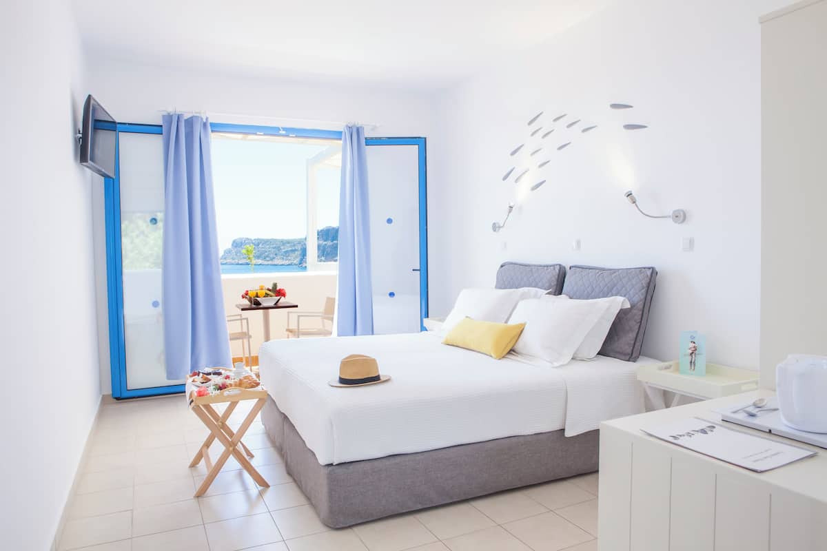 A modern hotel room with a bed, a small desk, a chair, and a view of the outdoors.