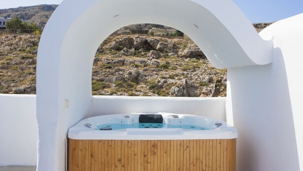 Un jacuzzi con interior de madera, frente a una pared exterior blanca, con vistas a un paisaje rocoso.