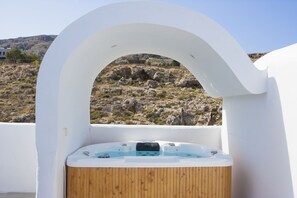 A hot tub with a wooden interior, set against a white exterior wall, overlooking a rocky landscape. - Lindos Sun (Rhodes)
