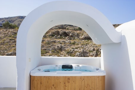 A hot tub with a wooden interior, set against a white exterior wall, overlooking a rocky landscape.