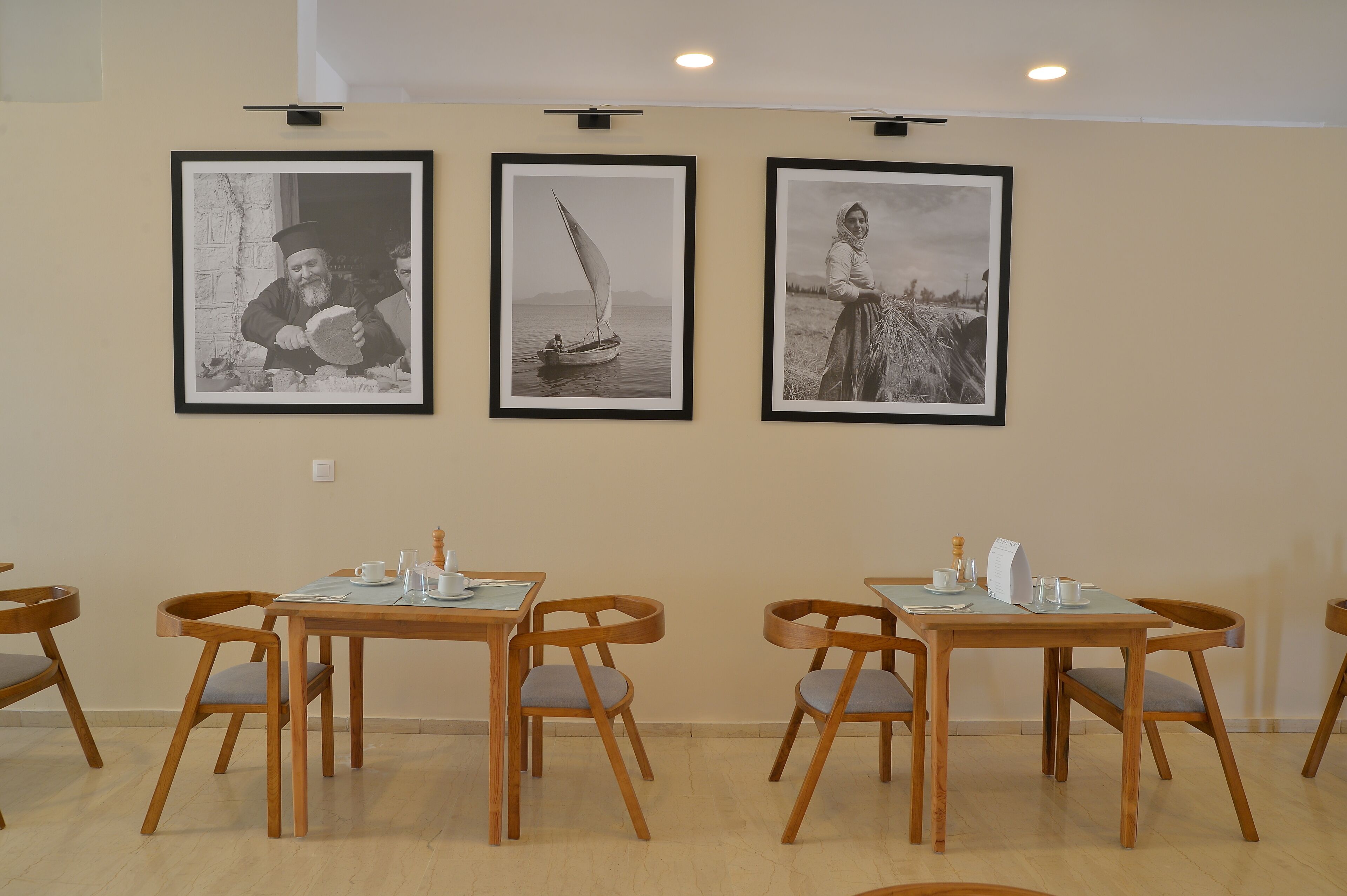 A dining area with wooden tables and chairs, framed black and white photographs on the wall, and a ceiling light.