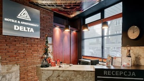 A hotel reception area with a marble counter, a Christmas tree, and a sign for Hotel & Apartment Delta. - Hotel Delta (Kraków)