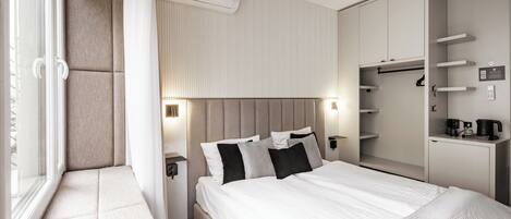 A modern hotel room with a bed, bedside tables, a wardrobe, and an air conditioning unit.