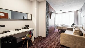 A hotel room with a desk, chair, bed, and a view of the city. - Hotel Delta (Kraków)