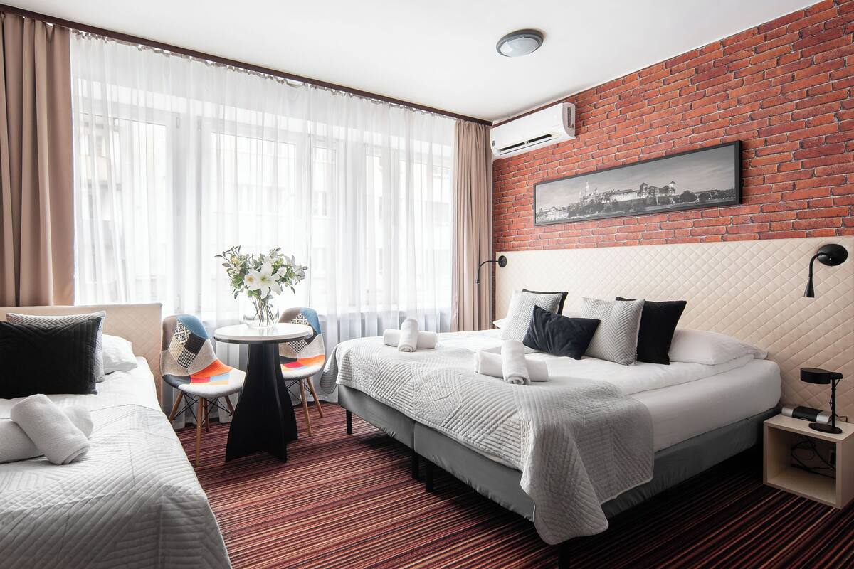 Une chambre d’hôtel avec deux lits, une petite table avec des chaises, une plante en pot et un mur en briques.