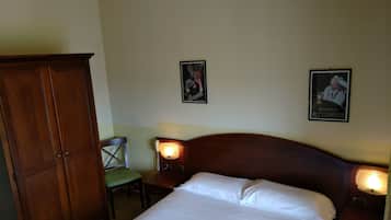A hotel room with a large wooden wardrobe, a single bed with white linens, two bedside tables with lamps, and two framed pictures on the wall.
