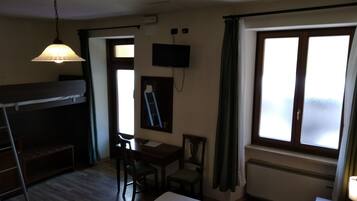 Una habitación con literas, un escritorio, una silla, un televisor montado en la pared y una ventana con cortinas.