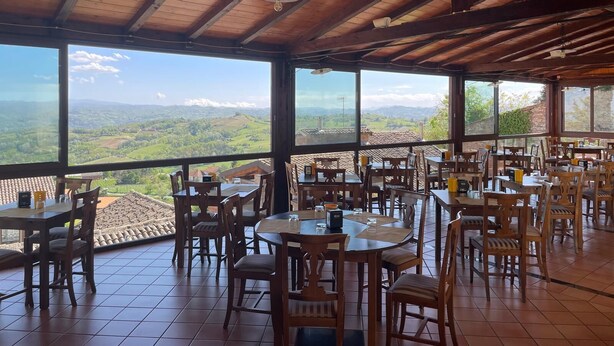 A restaurant with wooden tables and chairs, large windows offering a view of the countryside. - Hotel Belvedere (Alice Bel Colle)