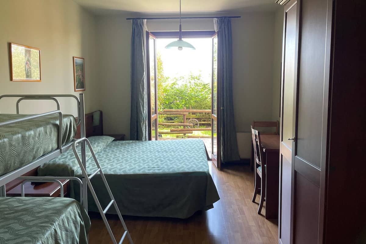 Une pièce avec deux lits superposés, un bureau en bois, une chaise, une échelle et une grande fenêtre avec des rideaux.