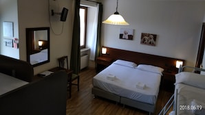 A hotel room with a bed, bedside tables, a desk, a chair, a mirror, a window with curtains, and a hanging lamp. - Hotel Belvedere (Alice Bel Colle)