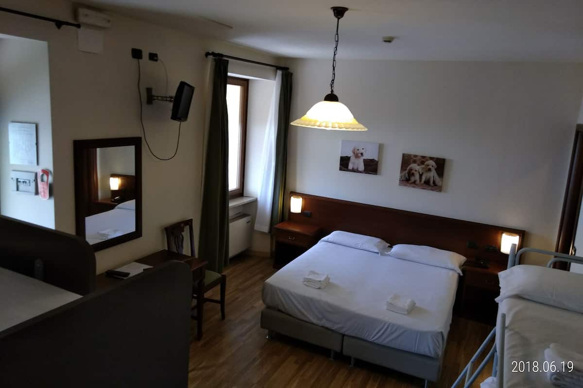 Une chambre d’hôtel comprenant un lit, des tables de chevet, un bureau, une chaise, un miroir, une fenêtre avec des rideaux et une lampe suspendue.