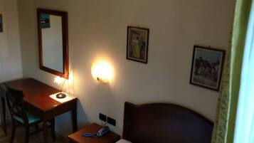 Una camera d'albergo con un letto, una scrivania con una sedia, una lampada e due quadri appesi al muro.
