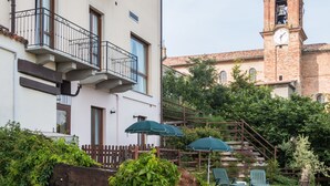 A hotel with a balcony, outdoor seating, and a clock tower in the background. - Hotel Belvedere (Alice Bel Colle)