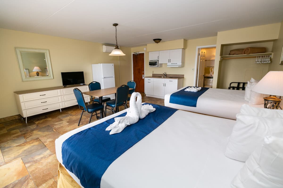 A hotel room with two beds, a desk, a chair, a television, and a kitchenette.