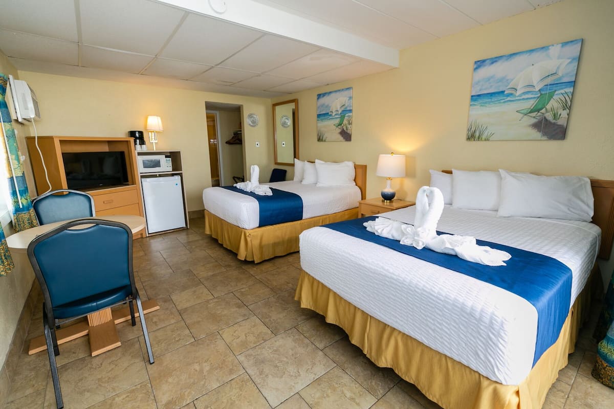 A hotel room with two beds, a desk, a chair, a microwave, and a small refrigerator.
