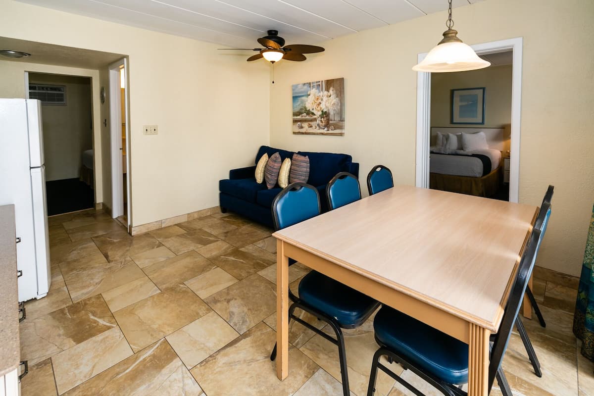 A dining area with a wooden table and blue chairs, a ceiling fan, and a painting on the wall.