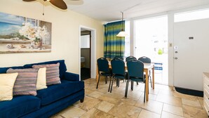 A living room with a blue sofa, a dining table with chairs, and a painting on the wall.