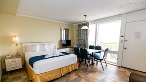 A hotel room with a bed, a desk, a TV, a dining table with chairs, and a balcony.