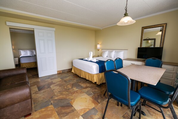 A hotel room with a bed, a desk with chairs, a television, and a mirror.