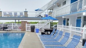 A swimming pool with lounge chairs and umbrellas, a covered deck area, and a view of the ocean.