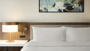 A neatly made bed with white bedding, a bedside table with a lamp, and a wall-mounted artwork.