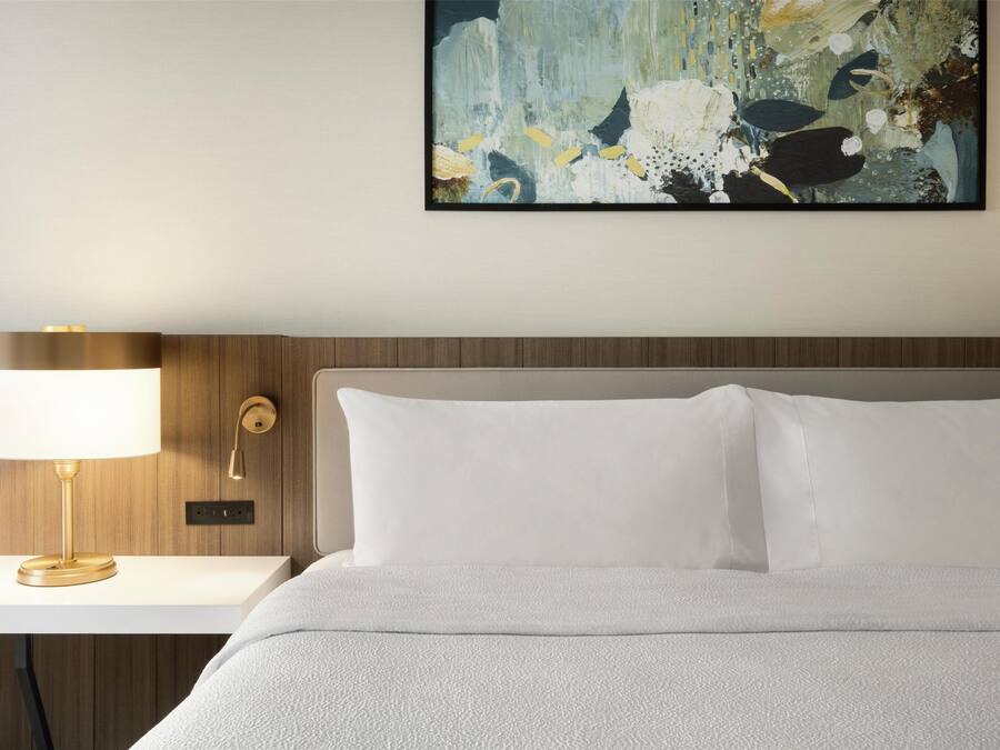 A neatly made bed with white bedding, a bedside table with a lamp, and a wall-mounted artwork.