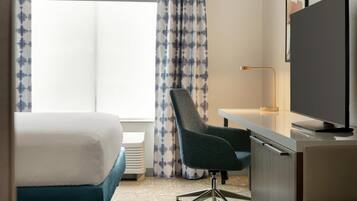 A hotel room with a bed, desk, chair, TV, and curtains.