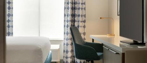 A hotel room with a bed, desk, chair, TV, and curtains.