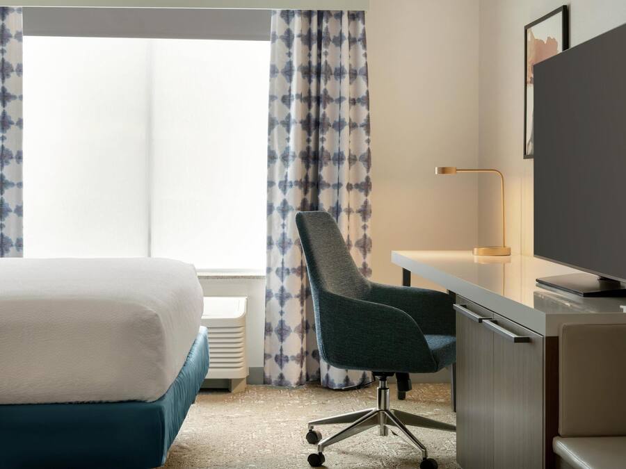 A hotel room with a bed, desk, chair, TV, and curtains.