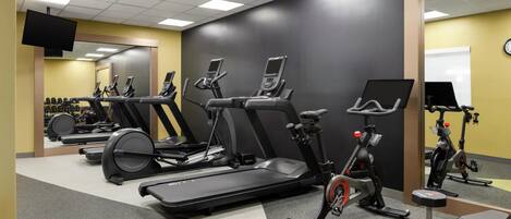Ein Fitnessraum mit Laufbändern, Crosstrainern und einer Gewichtshalterung.