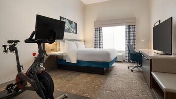 Habitación de hotel con cama, escritorio, silla, bicicleta estática, televisión y obras de arte en la pared.