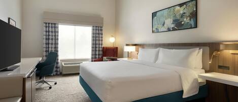 A hotel room with a large bed, a desk, a chair, a TV, a window with curtains, and a painting on the wall.