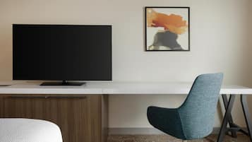 Een moderne hotelkamer met een groot flatscreen-televisie, een bureau met stoel en een lijst met een abstract schilderij aan de muur.