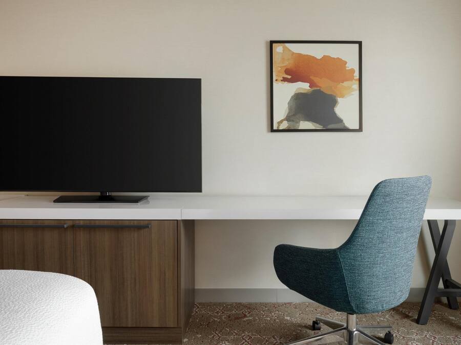 Een moderne hotelkamer met een groot flatscreen-televisie, een bureau met stoel en een lijst met een abstract schilderij aan de muur.