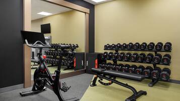 A gym with an exercise bike, a bench, and a rack of dumbbells.