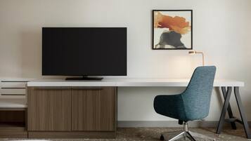 A modern office space with a flat-screen TV, a desk, a chair, and a framed abstract painting on the wall.