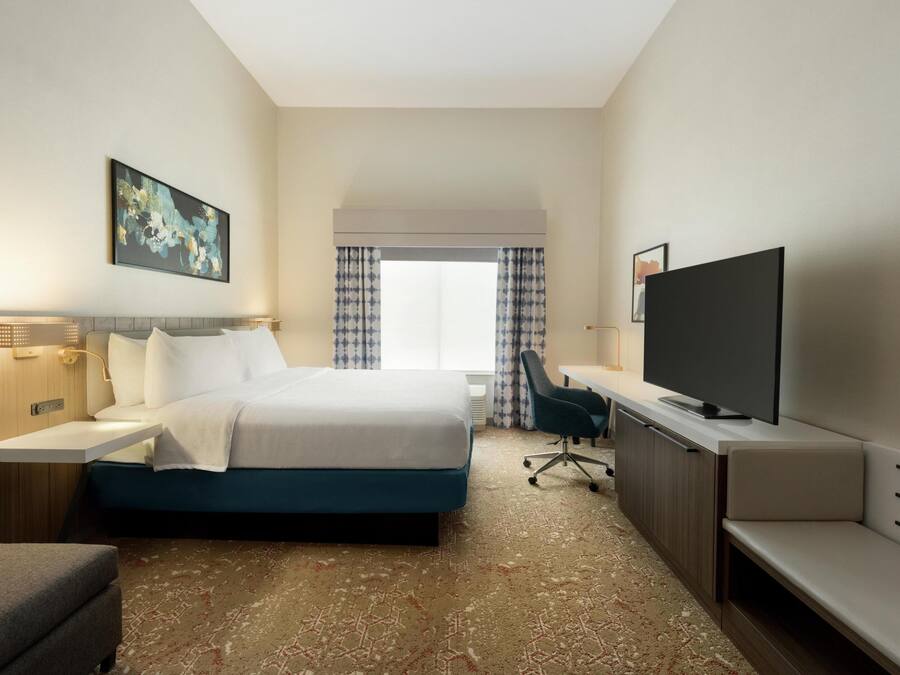 Habitación de hotel con cama, mesita de noche con lámpara, televisión y escritorio con silla.