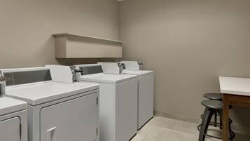 A laundry area with three washing machines and a drying rack.
