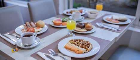 Una mesa de desayuno con platos de comida, un vaso de jugo de naranja y una taza de café.