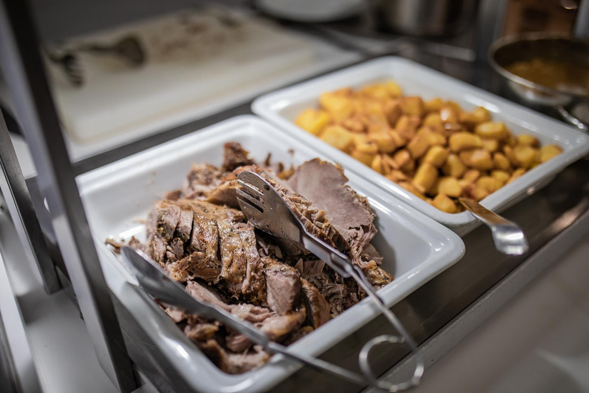 Een buffet met diverse gerechten, waaronder vleesschotel en aardappelen.