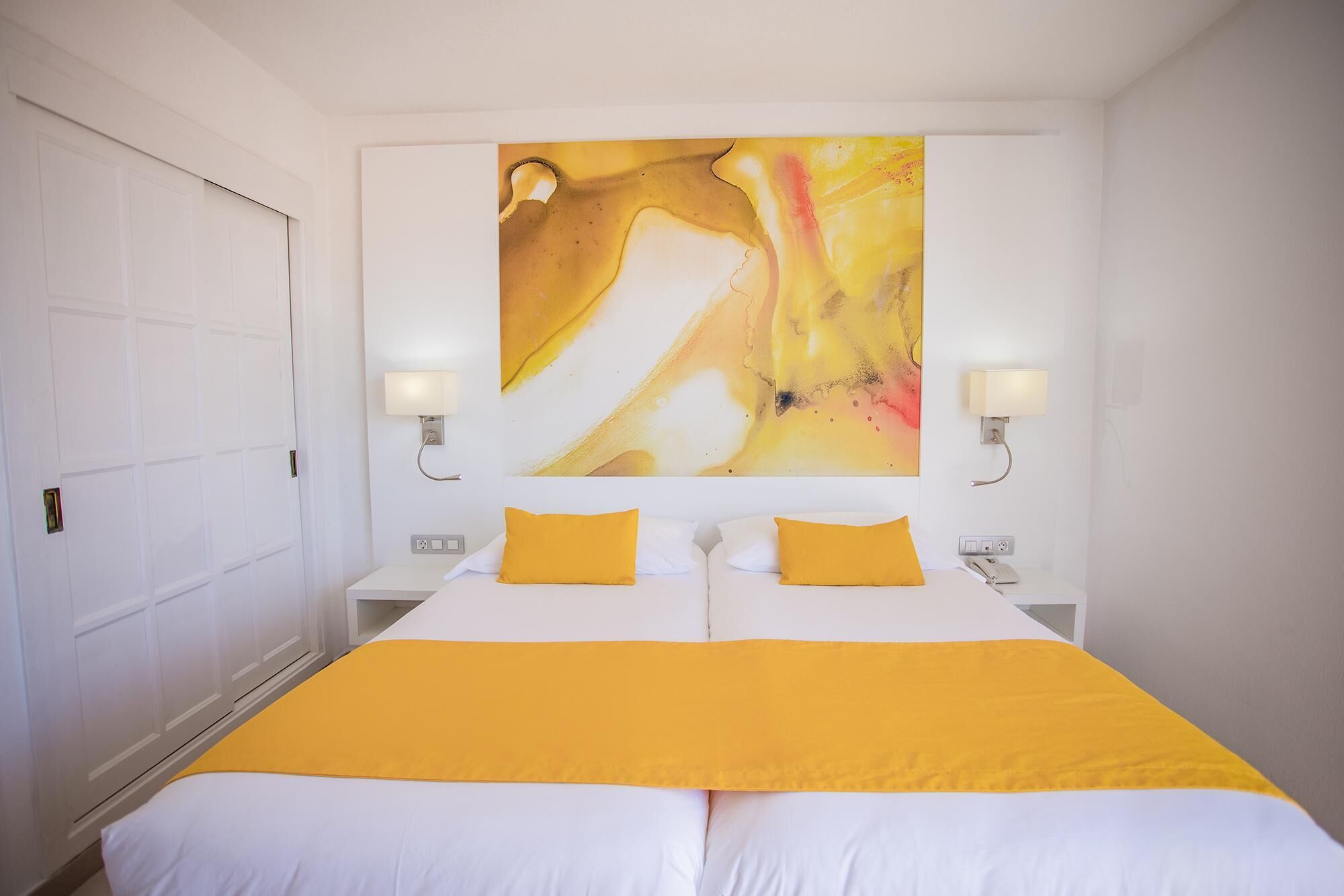 Habitación de hotel con una cama grande, dos mesitas de noche y un cuadro abstracto de gran tamaño en la pared.
