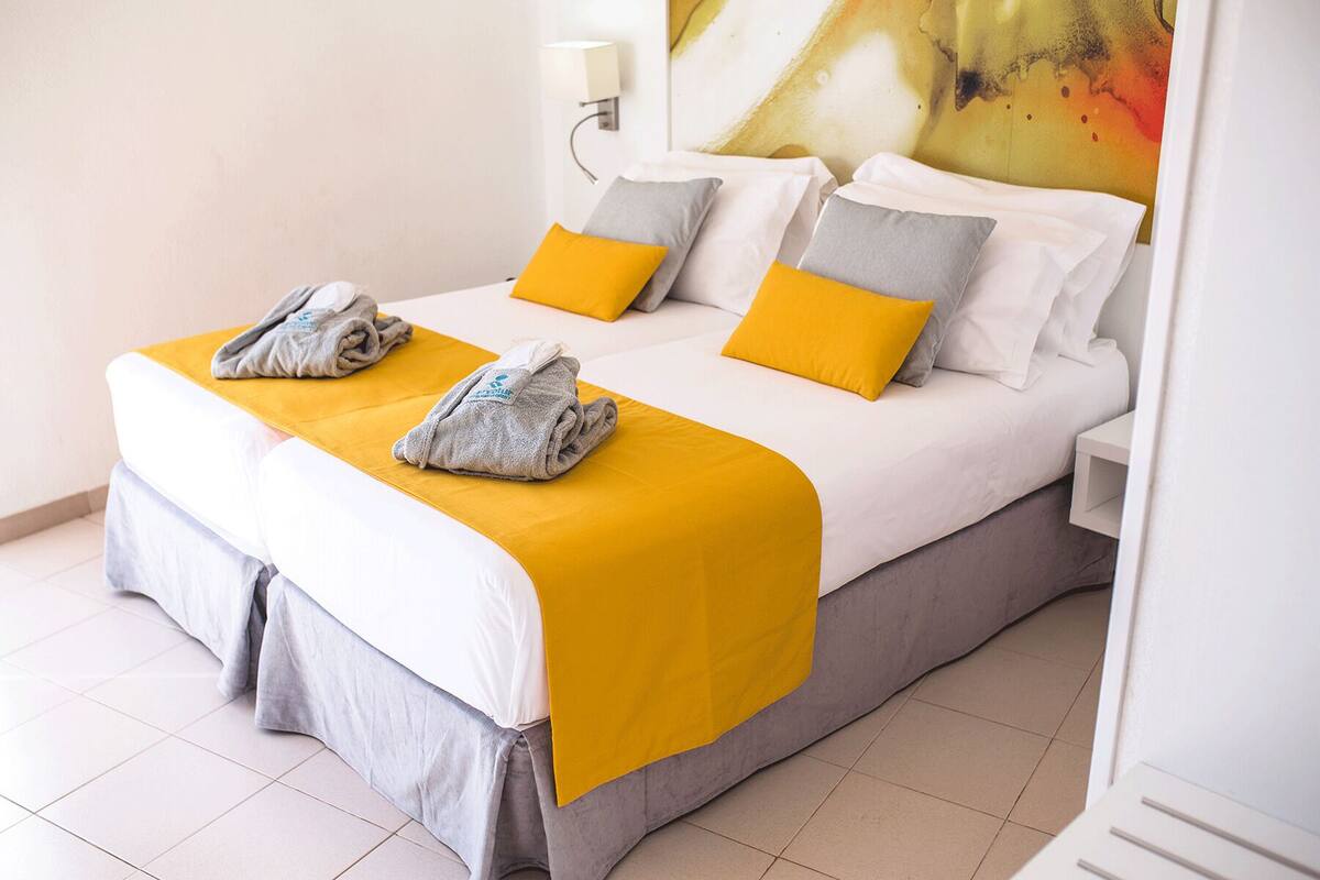 A double bed with a yellow and grey bedspread, two pillows, and two towels on the bed.