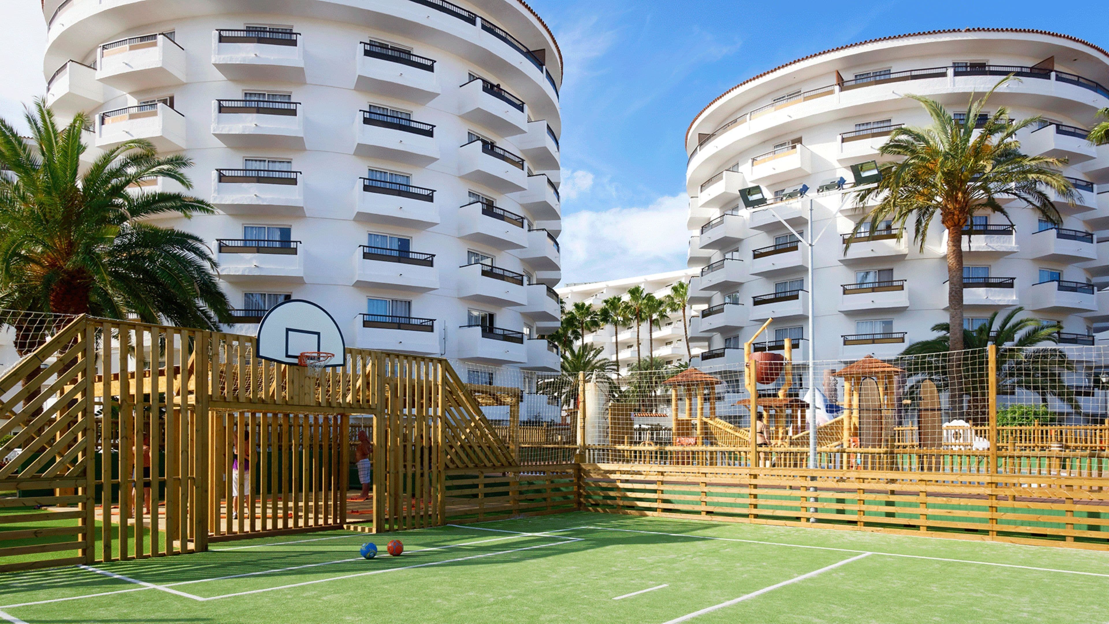 Un edificio de varios pisos con balcones y una cancha de baloncesto con valla de madera.