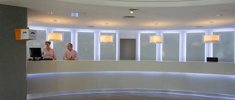 A modern reception area with a curved desk, two receptionists, and multiple pendant lights.