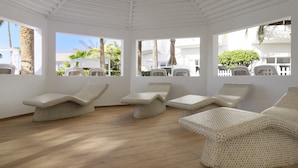 A sunroom with hexagonal patterned lounge chairs, large windows, and a wooden floor. - Servatur Waikiki (San Bartolomé de Tirajana)