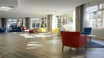 A spacious lobby with a wooden floor, large windows, and modern seating arrangements.
